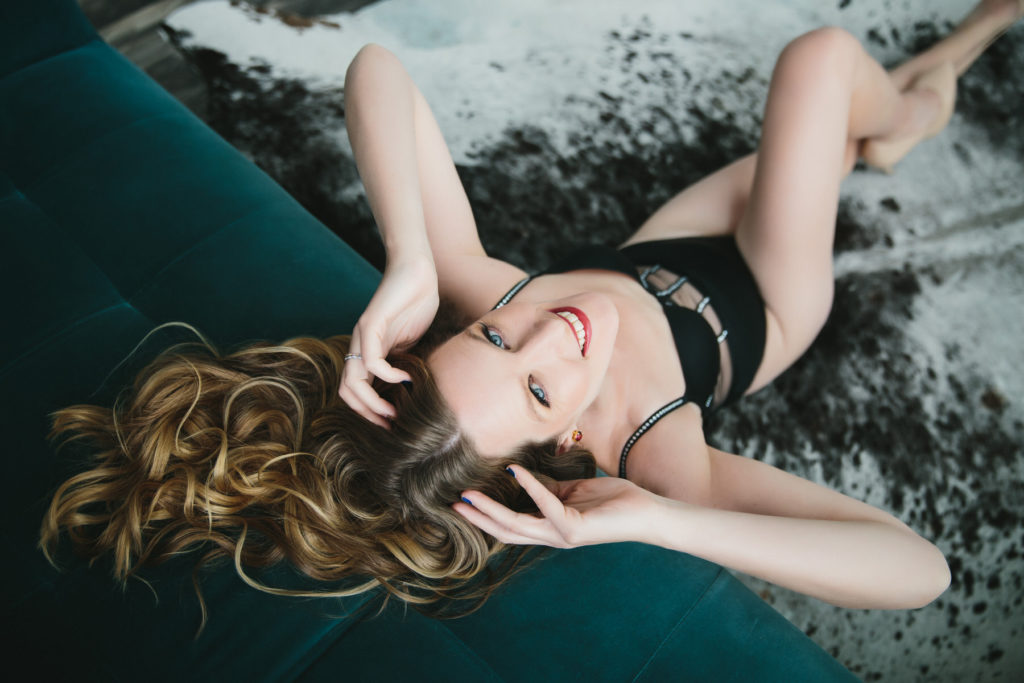 woman in black bodysuit on floor in front of teal sofa; boudoir photography by Lindsay Hite