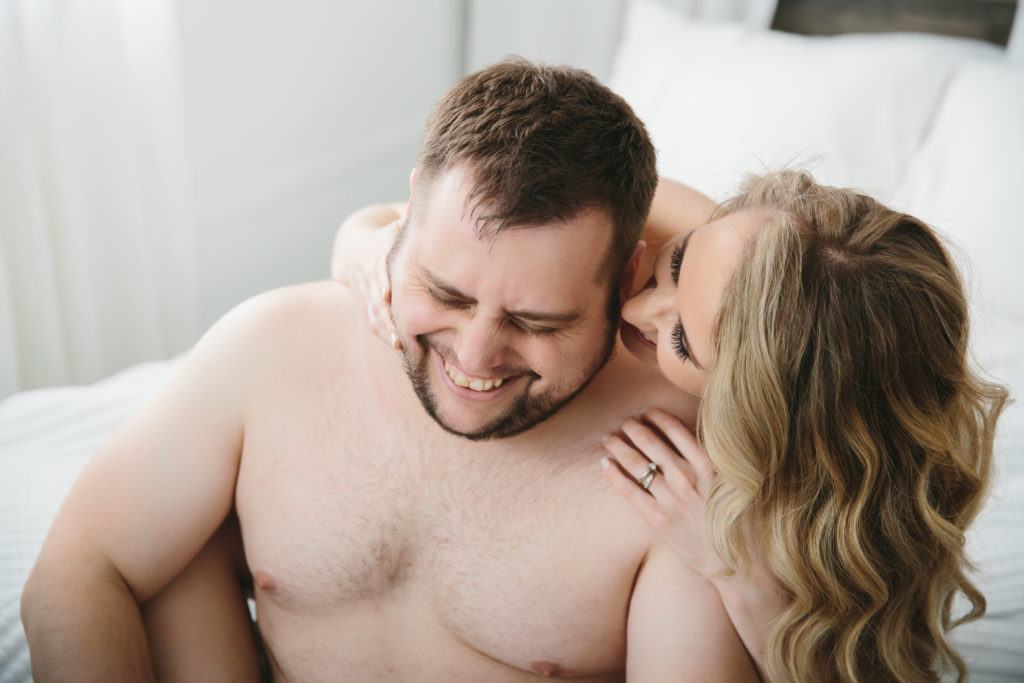 Topless couple laughing and smiling while sitting on bed; Couples Spark Session by Lindsay Hite