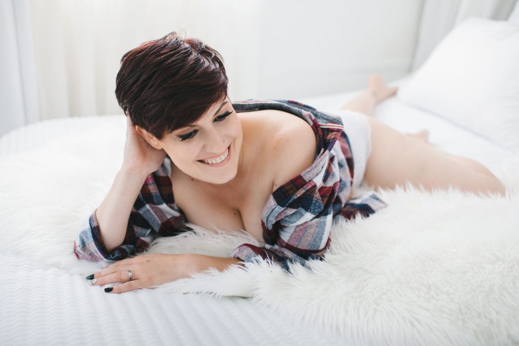 short haired woman in men's flannel shirt on fur lined bed; boudoir photography by Lindsay Hite