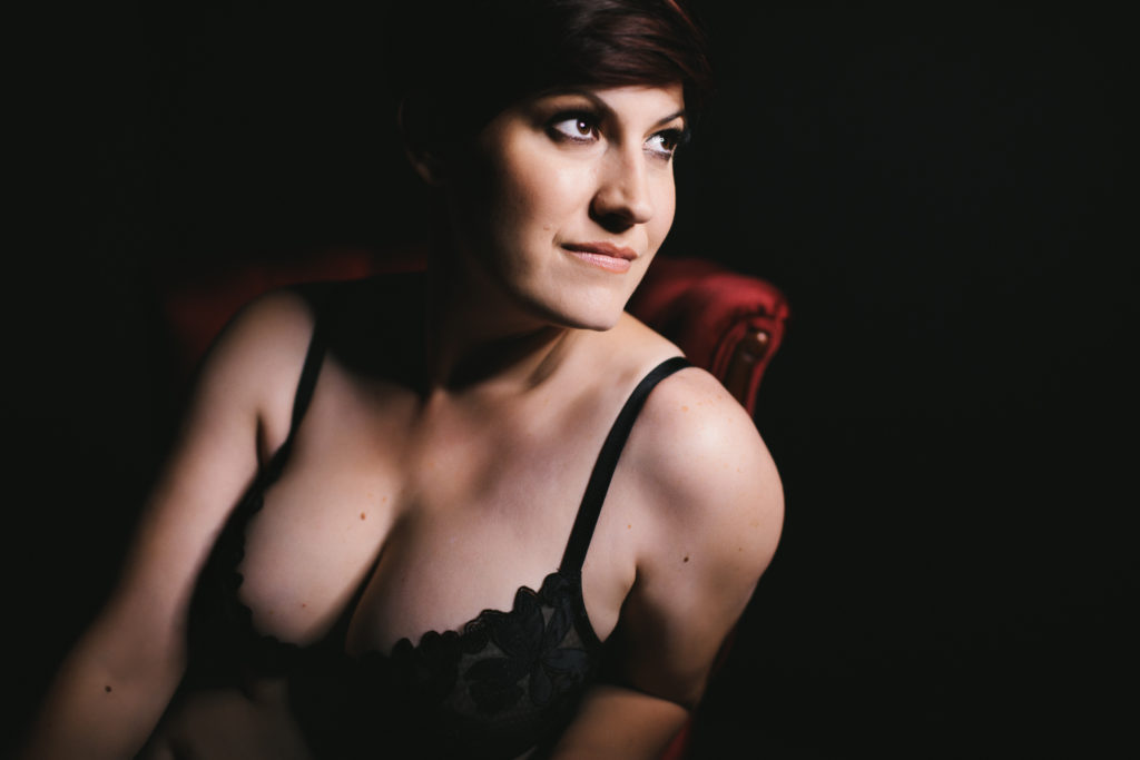 woman in black bra on red chair with black background; photography by Lindsay Hite