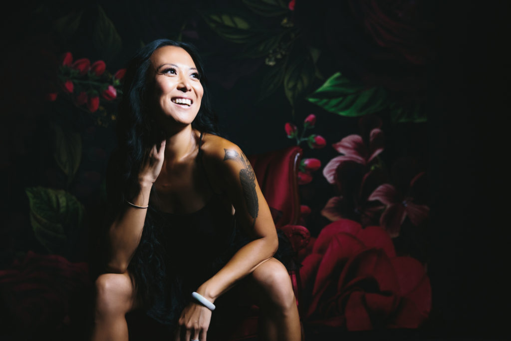 Asian woman smiling while seated in front of rose backdrop, photography by Lindsay Hite