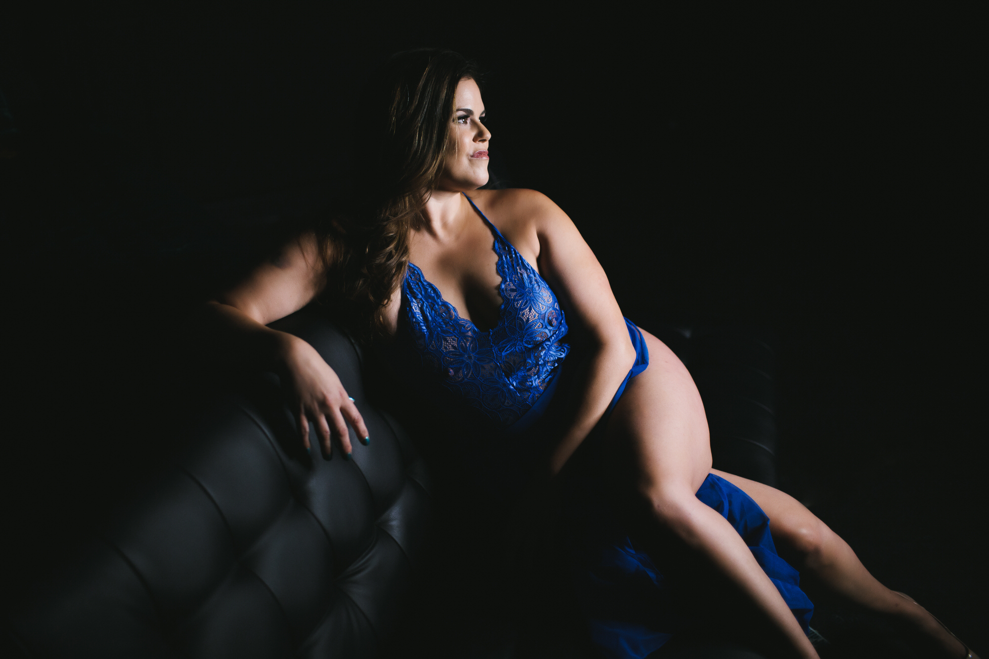 woman in blue lingerie with dark background on black sofa; by Lindsay Hite