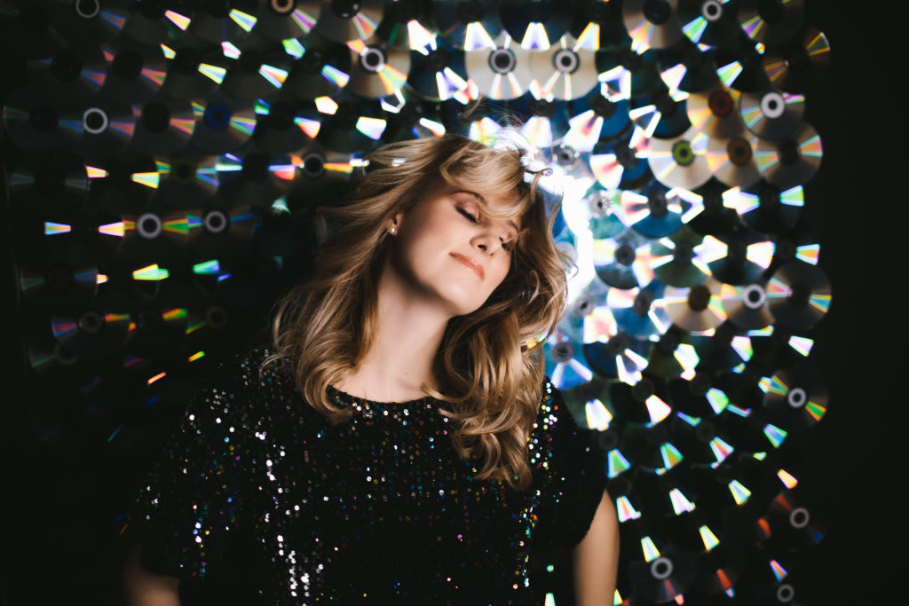 blond woman in sparkly black shirt in front of CD wall, boudoir photogrpahy by Lindsay Hite