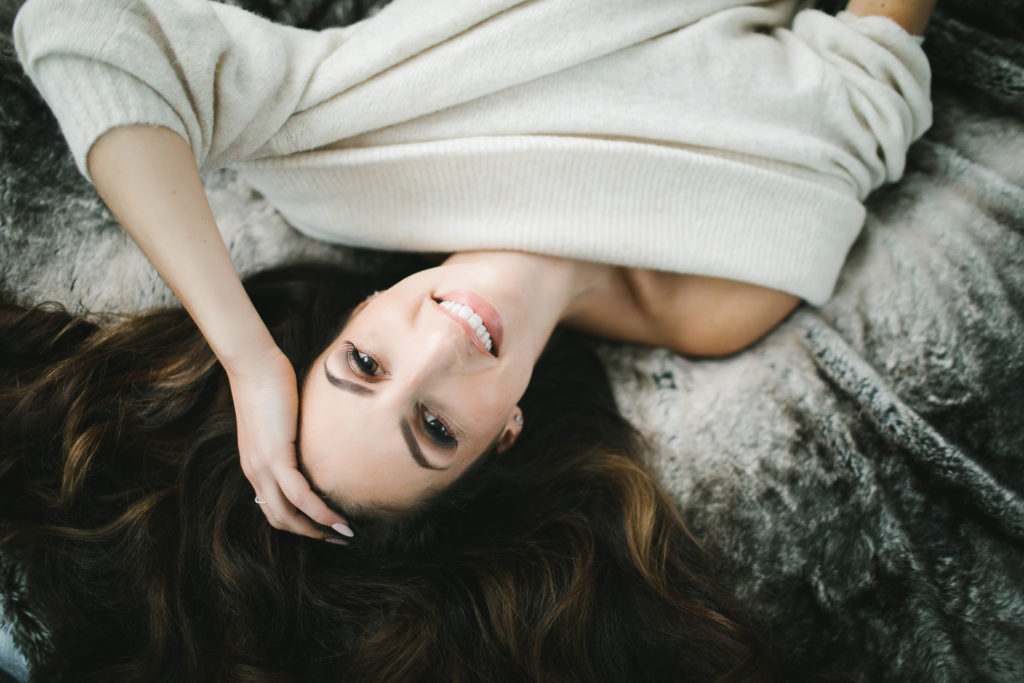 Woman in off-white sweater on bed. get naked for boudoir, photography by Lindsay Hite