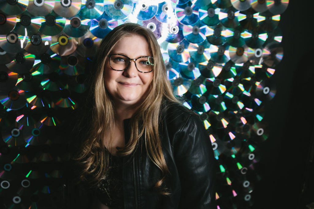 Woman with glasses in black leather jacket in front of a CD wall.  Photography by Lindsay Hite