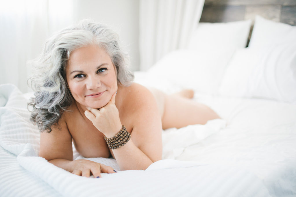 grey haired woman nude on white sheets; Boudoir Photography by Lindsay Hite