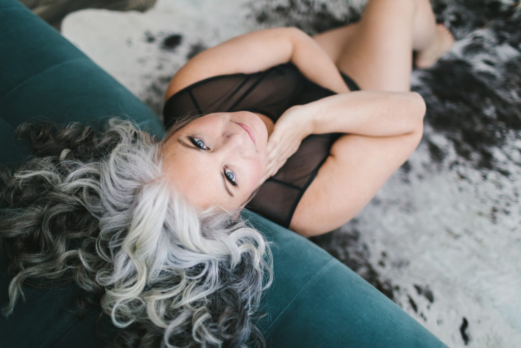 grey haired woman on teal sofa in black lingerie; Celebrate Their Journey With Boudoir Photography by Lindsay Hite