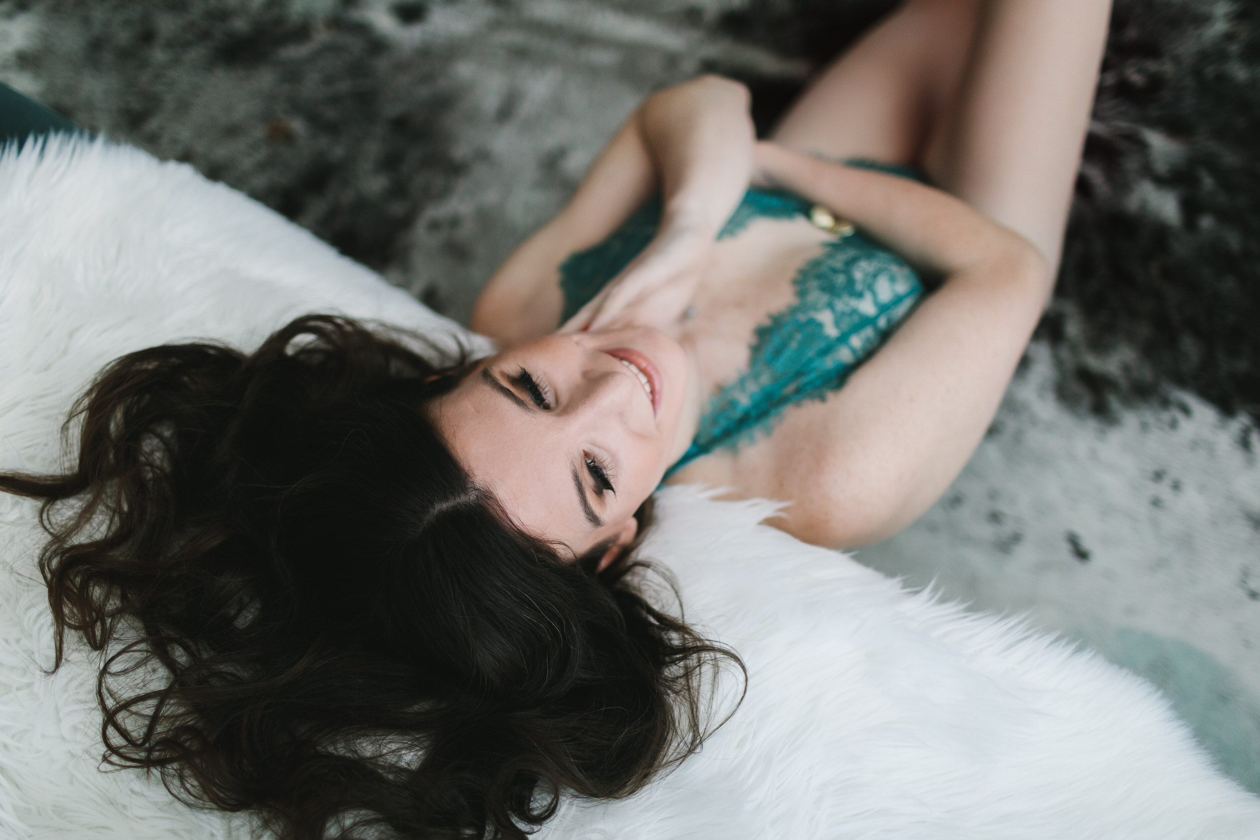 Woman in teal lingerie on white fur-lined sofa; embrace yourself through boudoir photography by Lindsay Hite