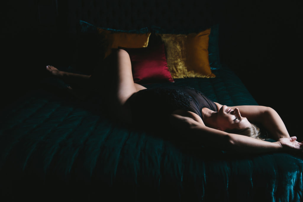 Woman in black lacey bodysuit on teal sofa with jewel-toned pillows; photography by Lindsay Hite