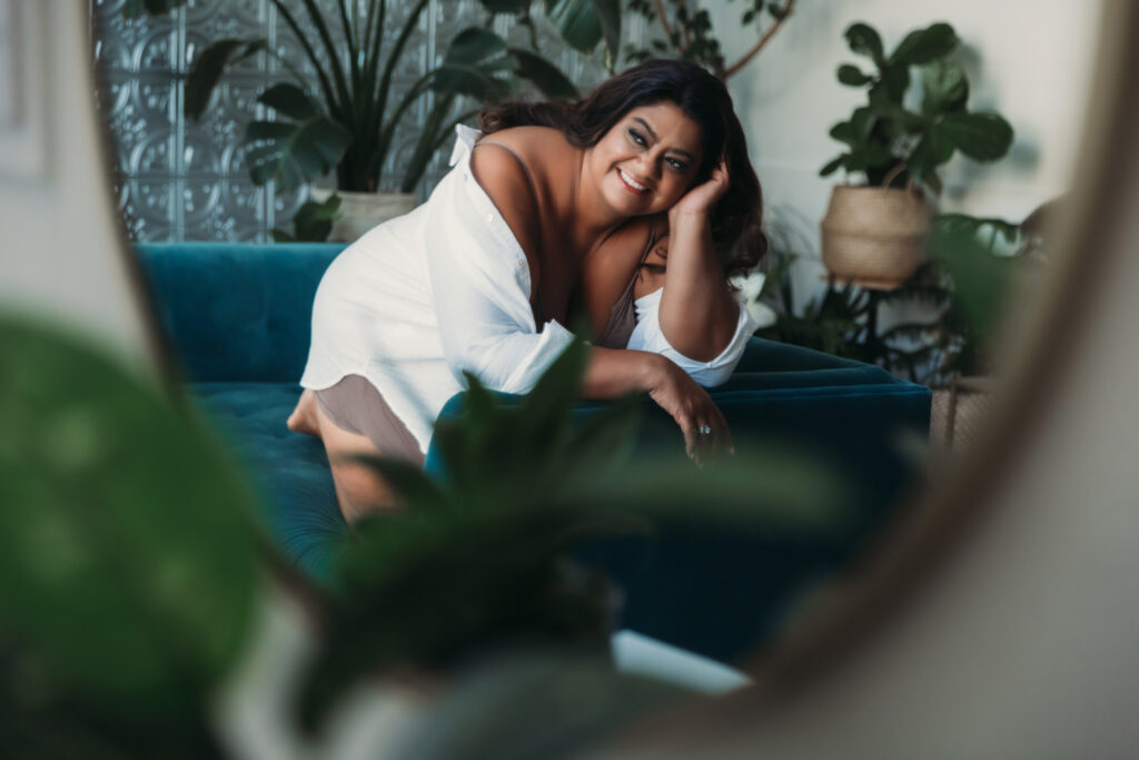 Boudoir Photography Myth:  I have to be a certain size for boudoir photography.  Woman posing in a button down white shirt on a teal sofa, By Lindsay Hite