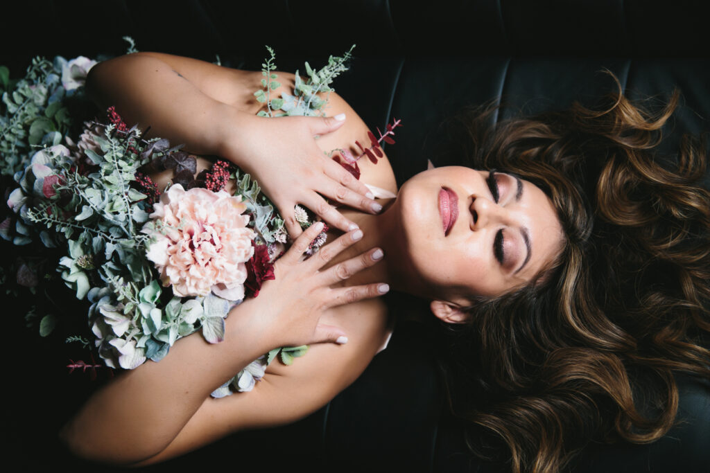 Woman on a black sofa with flowers on her chest.  Boudoir photography by Linsday Hite. 