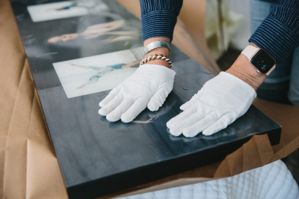 Woman wearing white gloves while inspecting wall art. Photography by Lindsay Hite