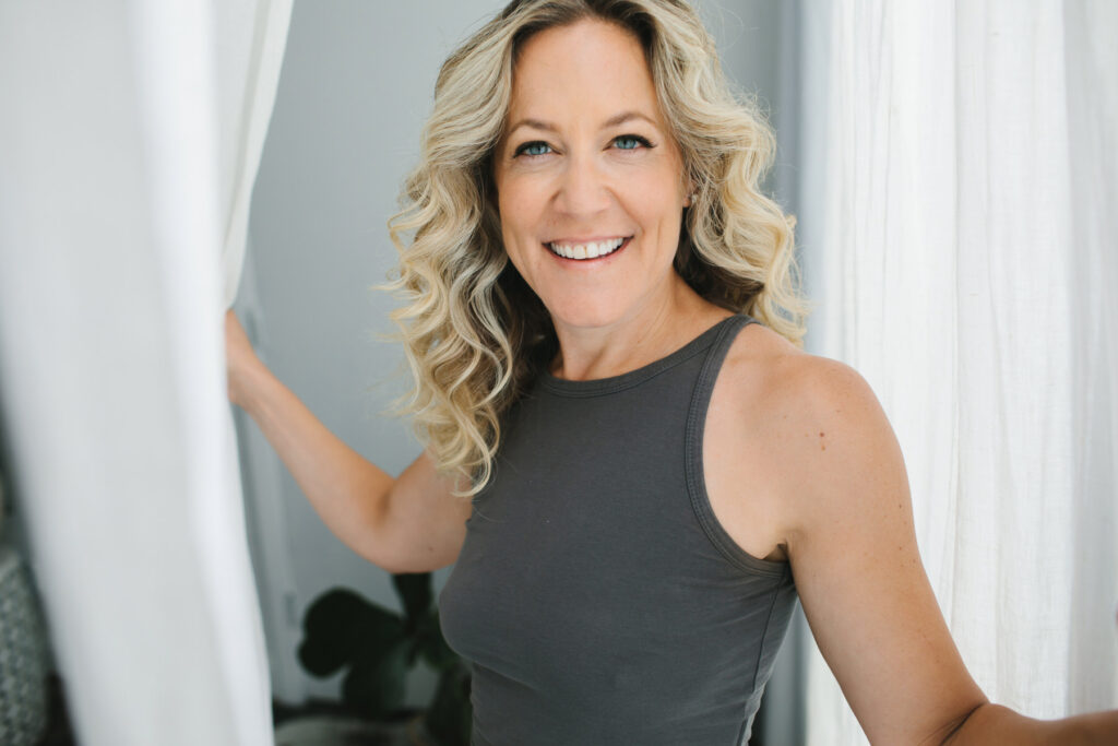 Blonde curly haired woman with natural makeup wearing grey t-shirt next to white curtains: Photography by Lindsay Hite Hair and Makeup by Michelle DeVoe