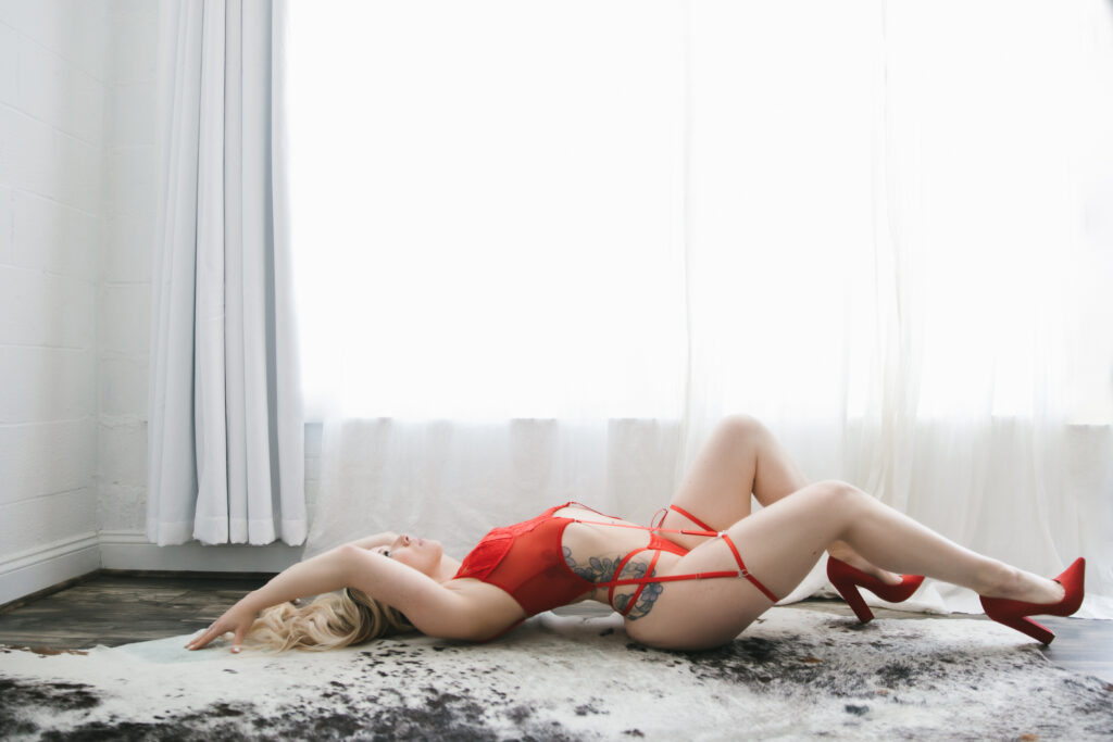 woman in red strappy lingerie on her back in front of white curtains, boudoir photography by Lindsay hite
