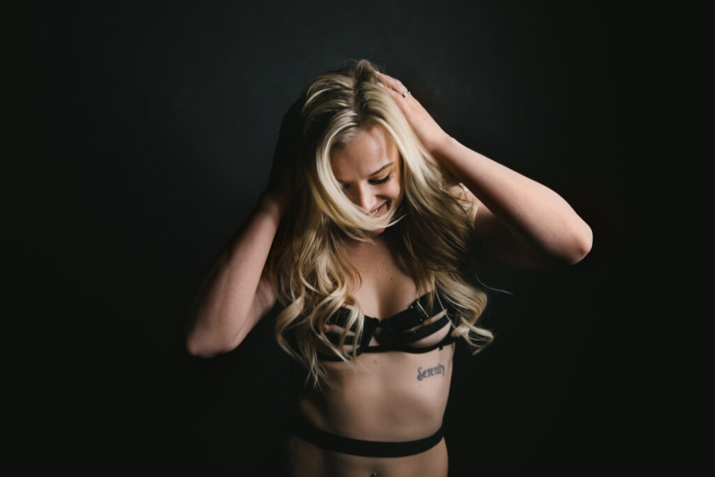 blond woman in black strappy lingerie against a black background, boudoir photography by Lindsay Hite