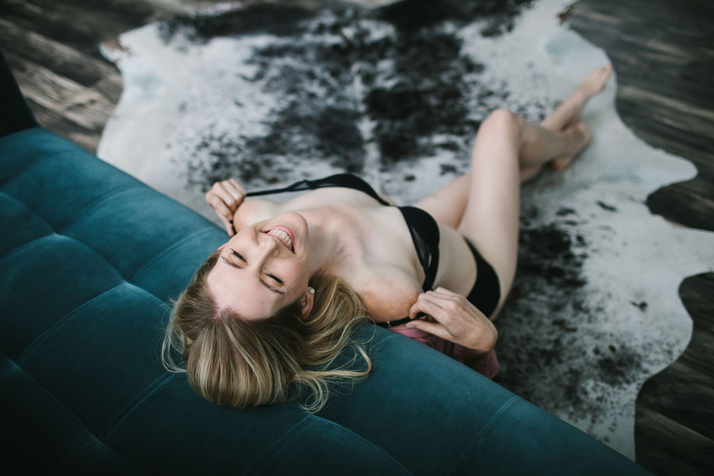 Blonde woman in black lingerie leaning against a teal sofa celebrating milestones of divorce and transition through boudoir photogrpahy