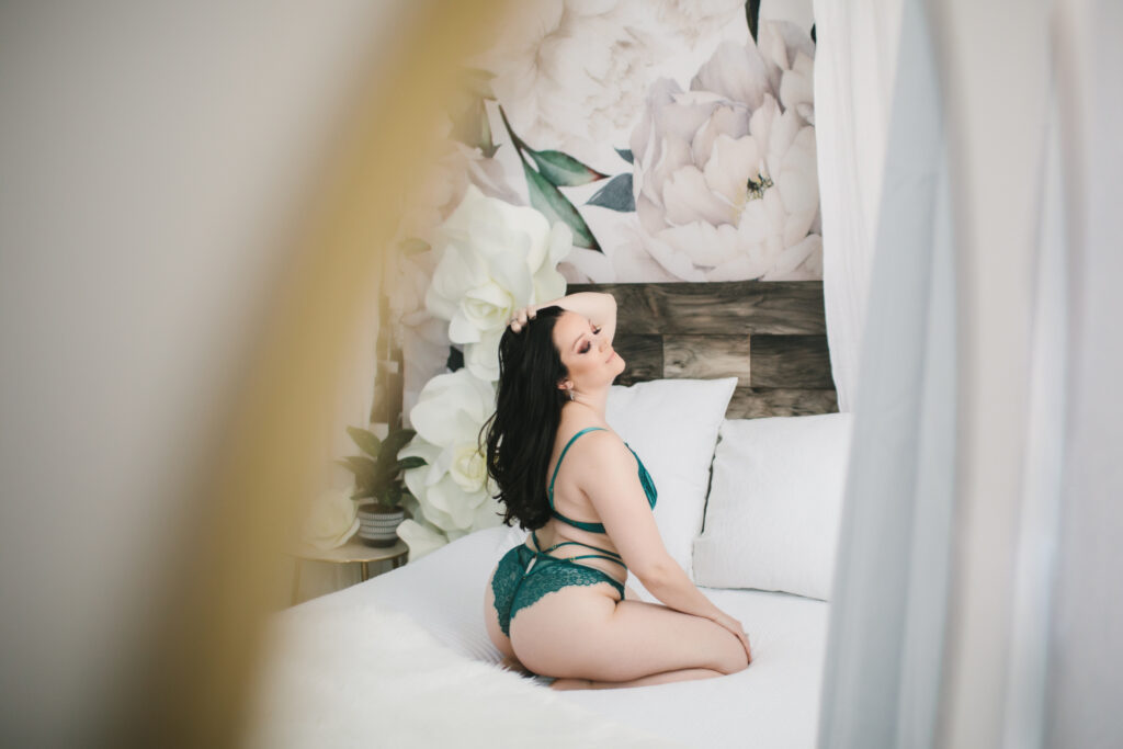 Zoomed out picture of a woman on her knees in green lingerie on a white bed.  Boudoir Photography by Lindsay Hite