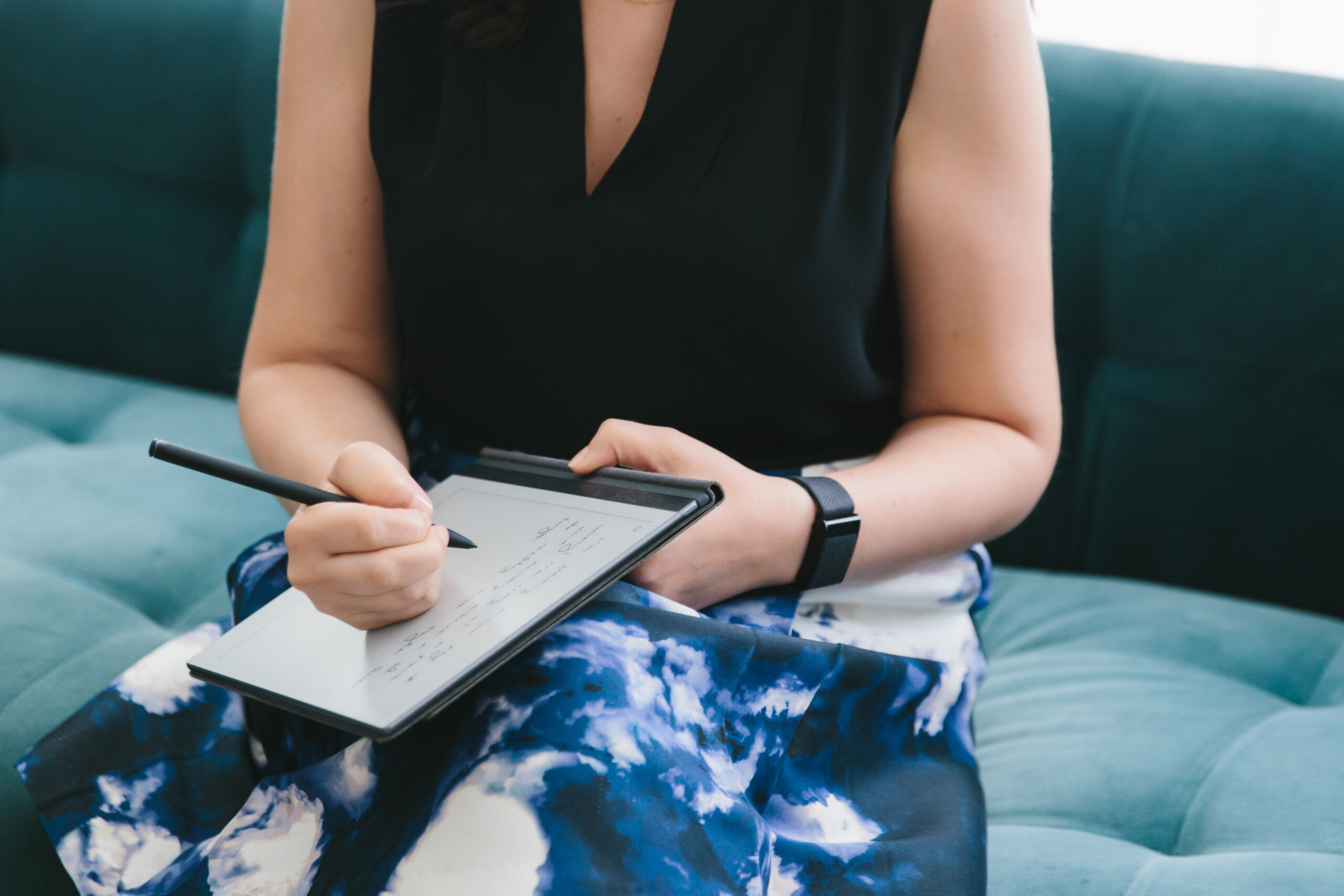 Portrait of a woman's torso sitting on a teal sofa writing in a notebook.  Photography by Lindsay Hite. 