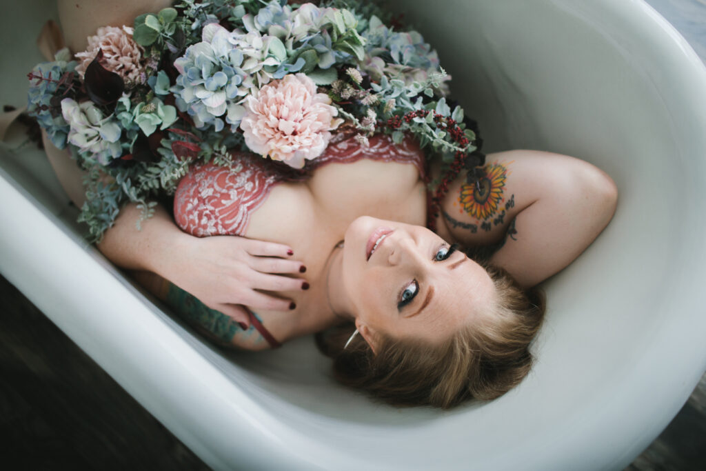 Woman in lacy pink and silver bra with flowers in a garden bathtub. Boudoir photography by Lindsay Hite. 