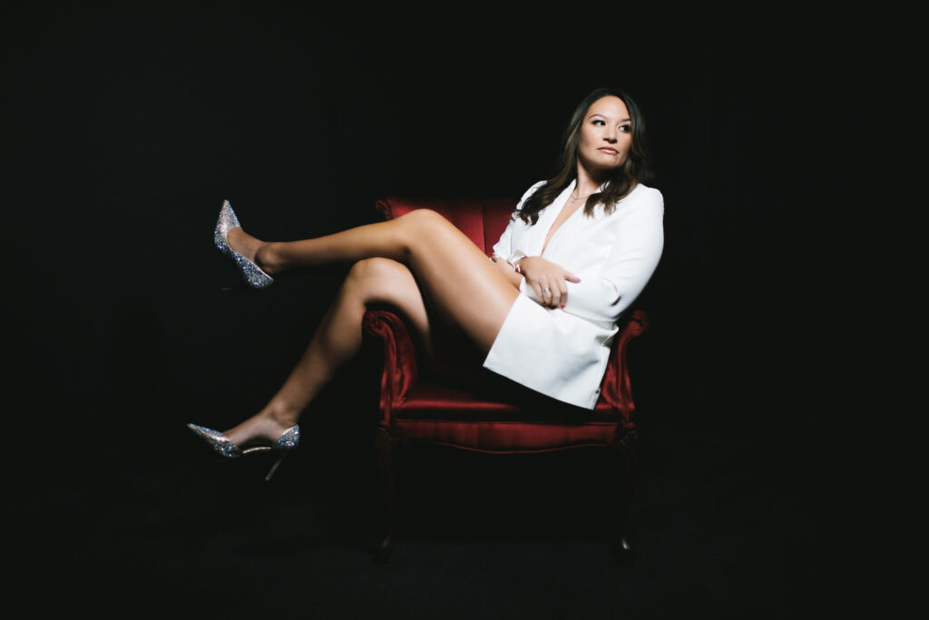 Woman sitting in a red velvet chair in a white jacket with silver sparkly shoes.  

Boudoir photography by Lindsay Hite. 