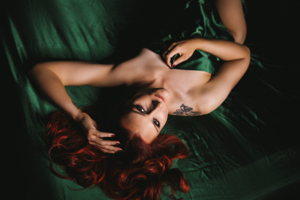 Woman with red hair in emerald satin sheets.  Boudoir photography by Lindsay Hite. 
