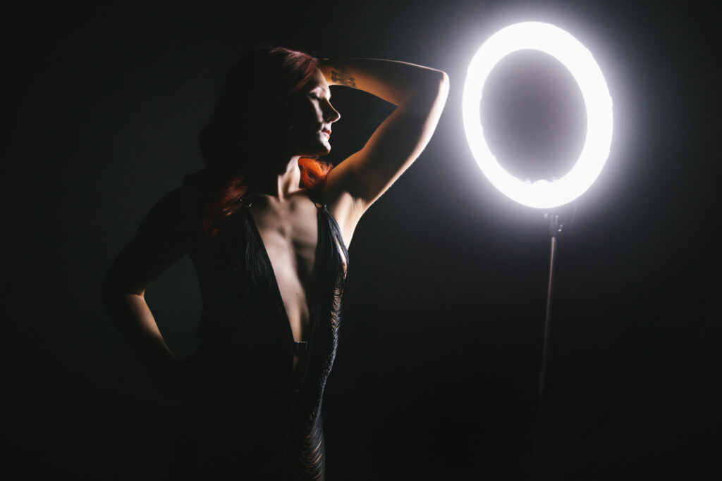 Woman celebrating milestones through boudoir photography in a black fringe dress with a black background and ring lighting. Boudoir photography by Lindsay Hite. 