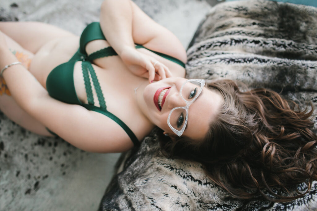 Brunette woman in emerald green bra leaning back on a fur-lined sofa.  Boudoir Photography by Lindsay Hite. 