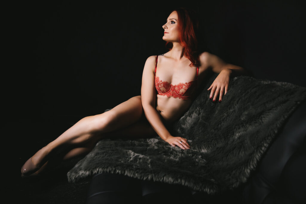 Woman in a fur line black sofa while wearing dark peach lingerie with a black background.  Photography by Lindsay Hite