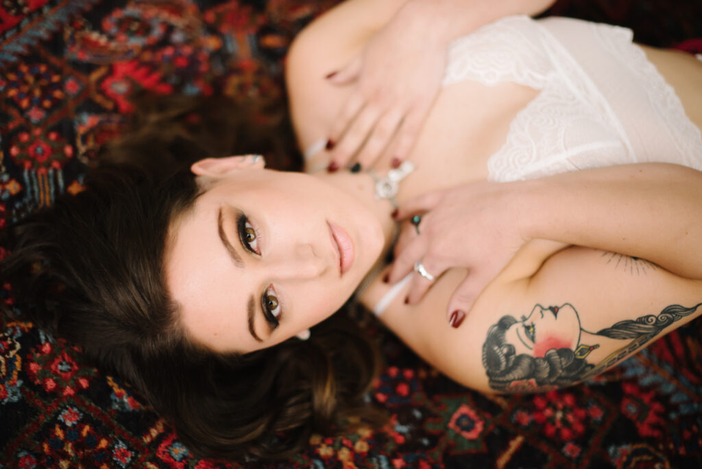 Brunette woman in white lacey bra laying on her back on a red oriental rug. Photography by Lindsay HIte.