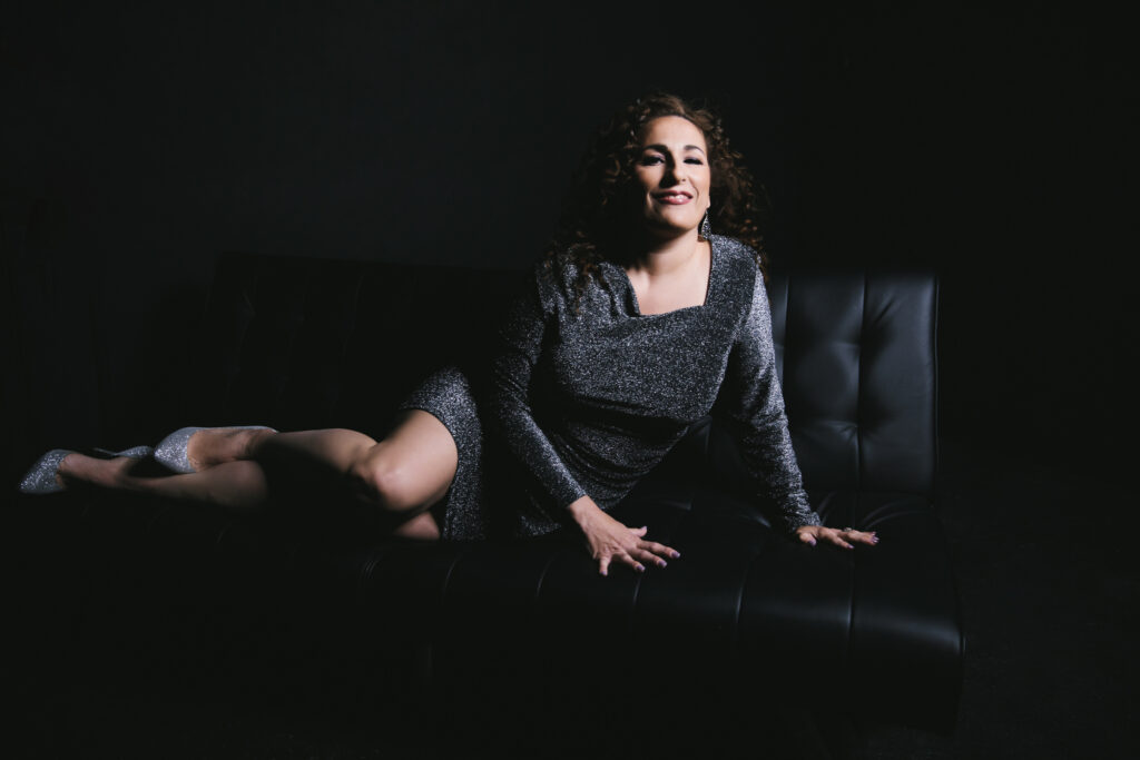Woman in sparkly black dress leaning on a black sofa with a black backdrop. Photography by Lindsay Hite at Show Your Spark