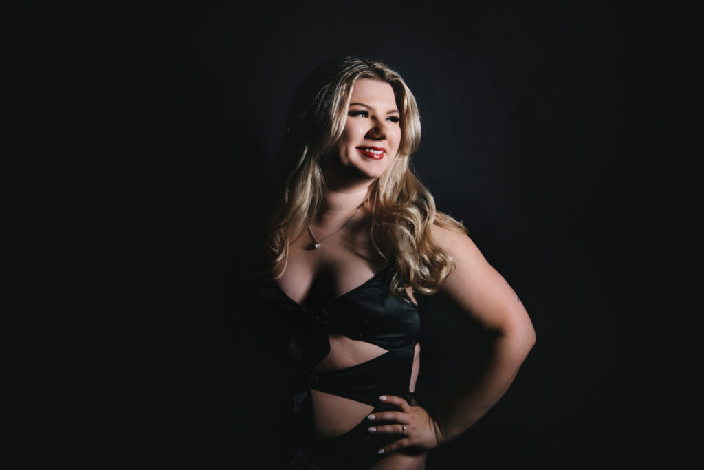 Blonde woman in black lingerie with a black backdrop. Photography by Lindsay Hite at Show Your Spark.