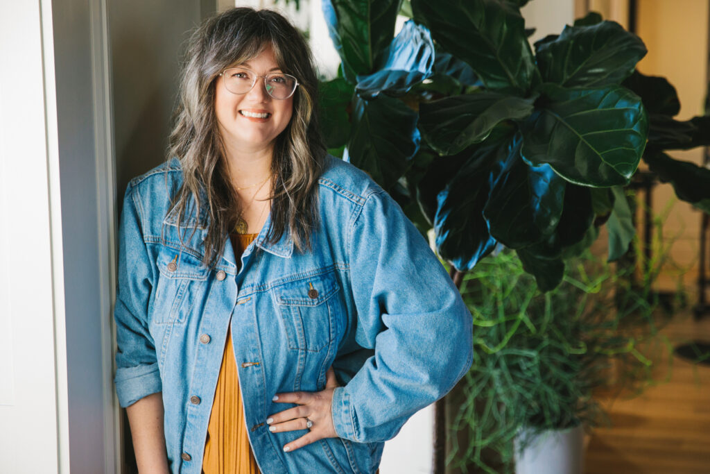 Casual headshot of a woman wearing an ochre colored dress with a denim jacket.  Photography by Lindsay Hite. 