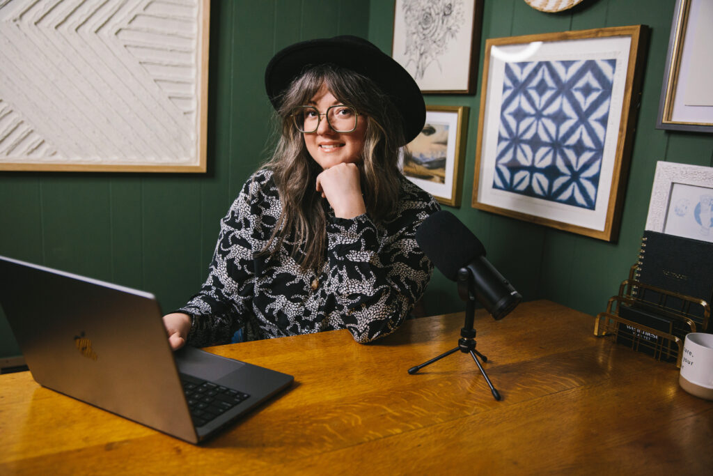 Woman wearing a black hat, sitting at her computer and podcasting microphone.  Branding photography by Lindsay Hite. 