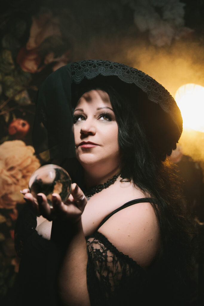Woman in black lingerie, a black hat, and crystal ball looking fierce & fine after forty.  Boudoir Photography by Lindsay HIte. 