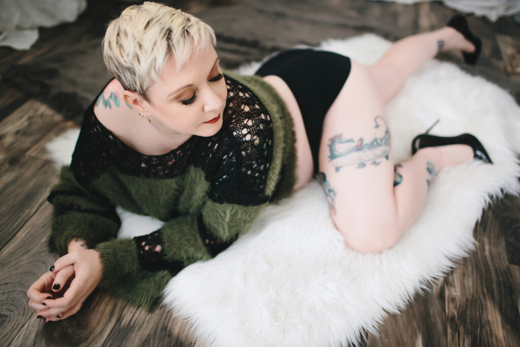 Woman in green and black sweater on a white fur blanket on a wooden floor.  Photography by Lindsay Hite