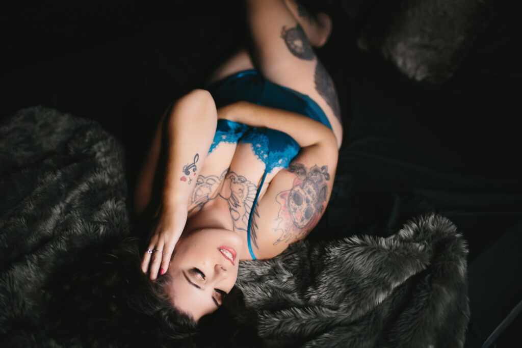 Woman in blue lingerie on a black fur-lined bed with a dark background. Photography by Lindsay Hite
