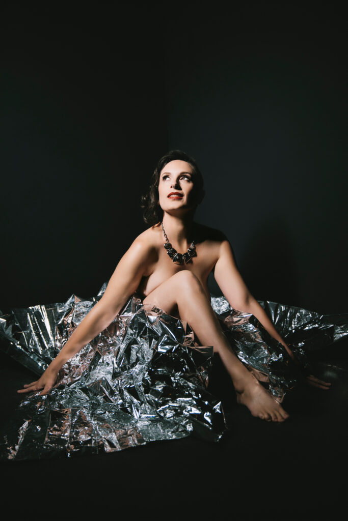 Woman sitting in a silver tutu with a black background.  Photography by Lindsay Hite
