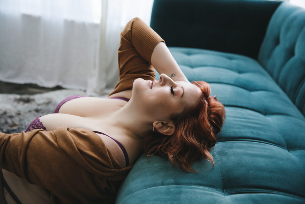 Woman in purple bra and brown cardigan leaning back on a teal sofa.  Photography by Lindsay Hite