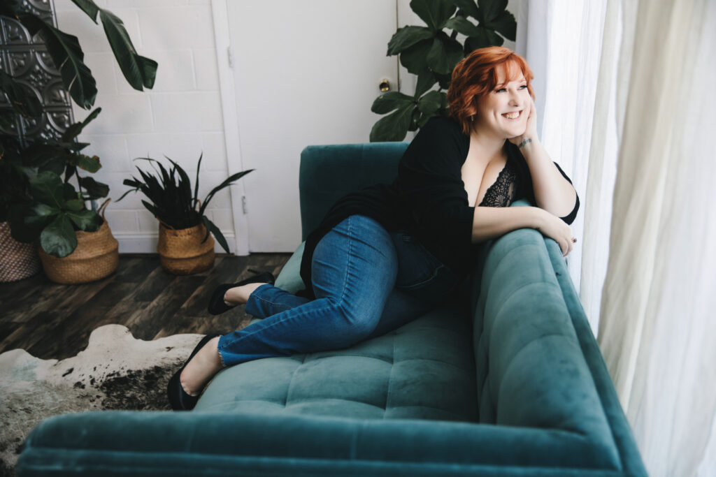 Woman in black top and jeans in a teal sofa looking out the window. Photography by Lindsay Hite