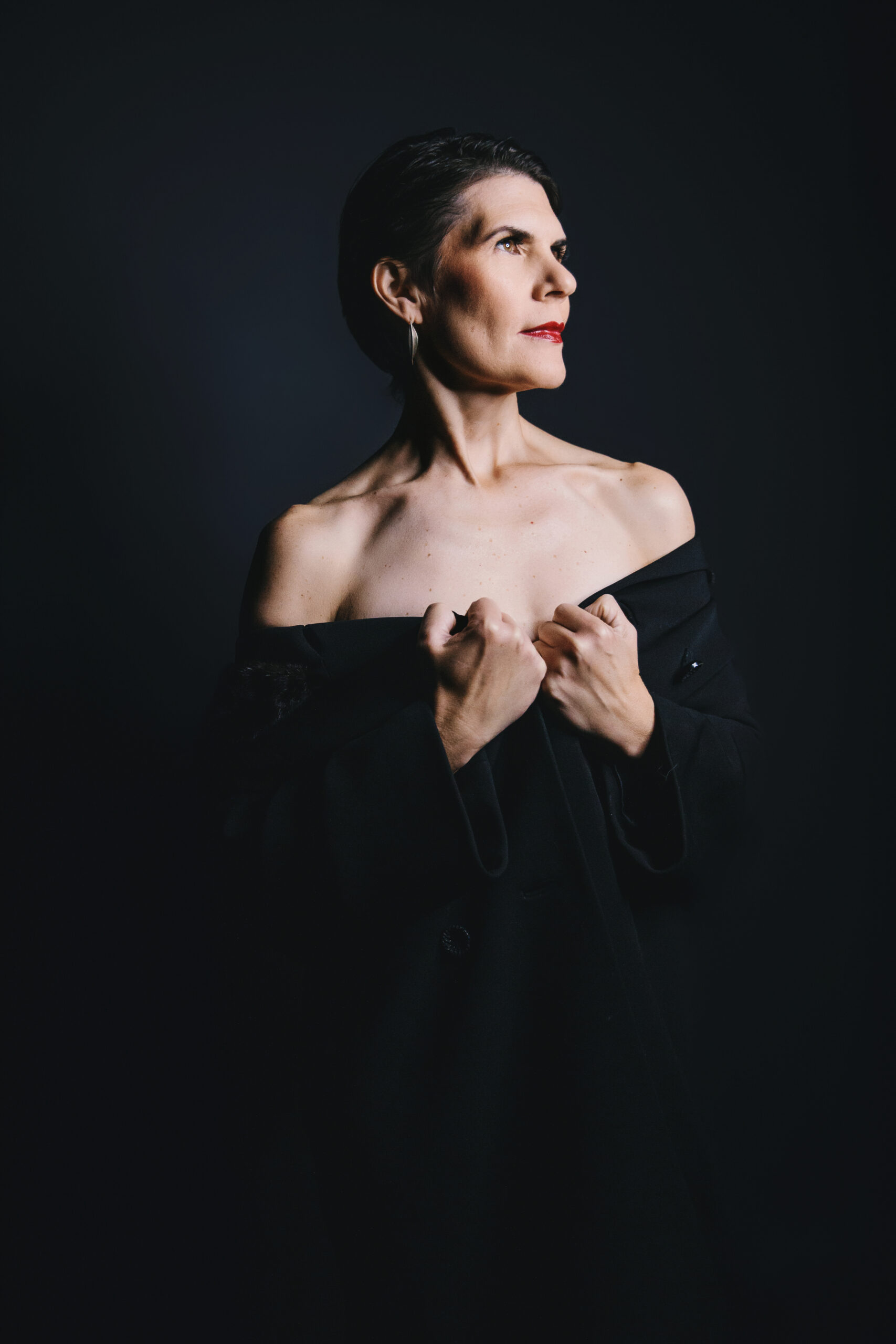 Woman in black off shoulder top with black background shows how to age well after forty. Photography by Lindsay Hite.