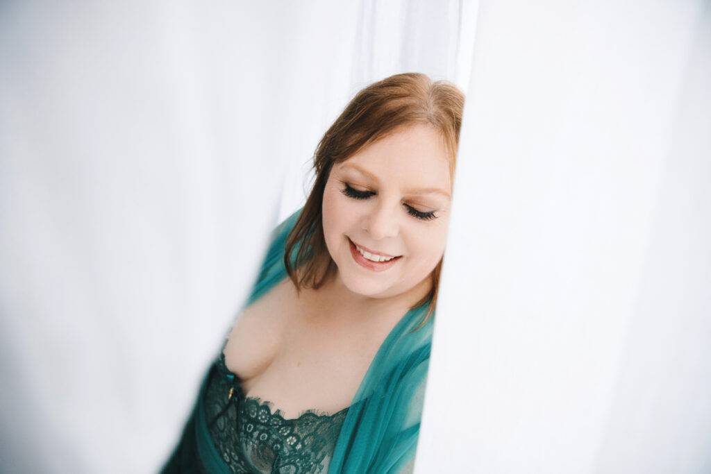 Woman in teal lingerie behind a white curtain- a fierce and unstoppable woman over forty.  Photography by Lindsay Hite. 
