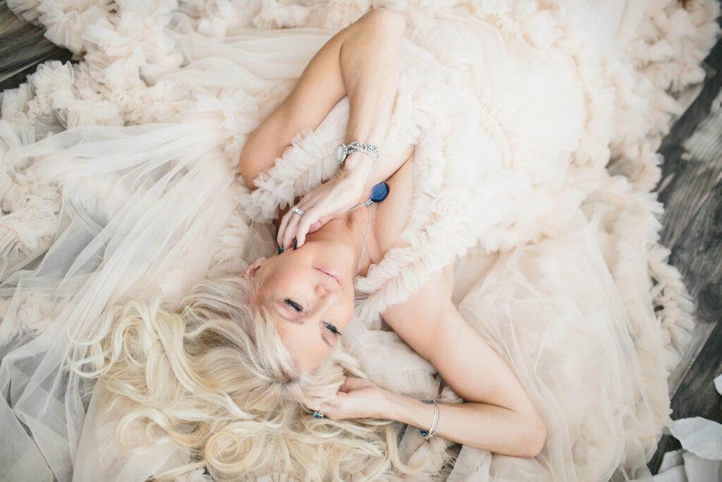 Woman in ruffled off-white dress laying on the ground.  Photography by Lindsay Hite. 