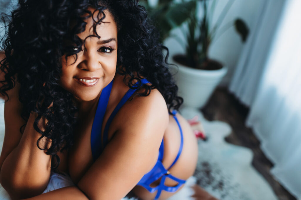 African American woman in blue strappy lingerie leaning against a sofa with plants in the background. Photography by Lindsay Hite