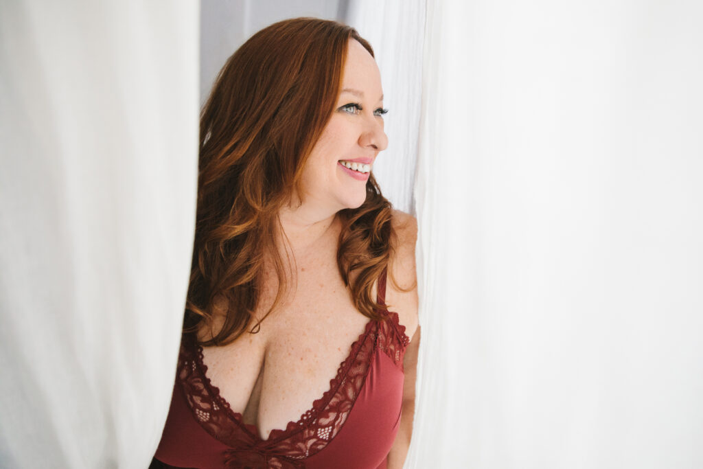 Woman in red lingerie peaking through white curtains. Photography by Lindsay Hite.