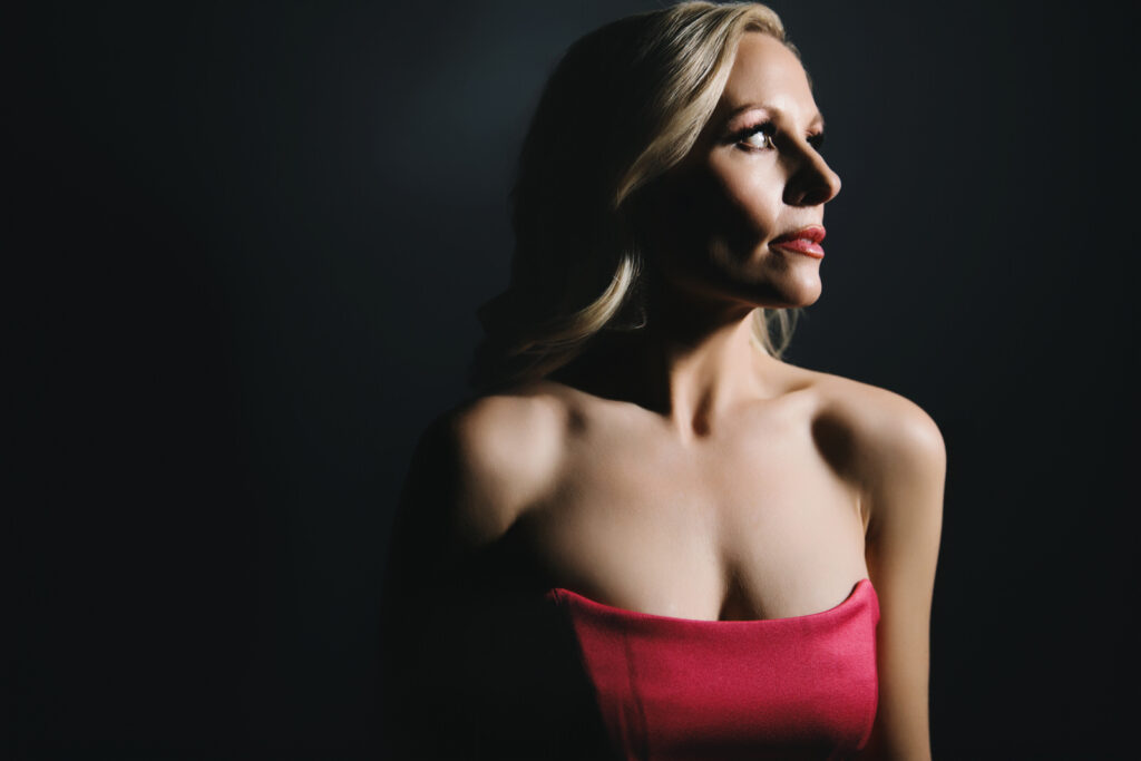 Woman in sleeveless pink dress looking away from the camera against a black background.  Photography by Lindsay Hite. 