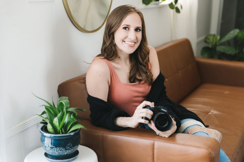 Branding session portrait of a photographer sitting on a leather couch holding her camera.  Photography by Lindsay Hite. 