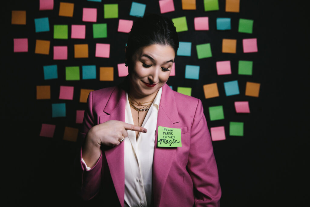 Branding session portrait of a woman wearing a white shirt and pink blazer with sticky notes on a black background.  Photography by Lindsay Hite.  