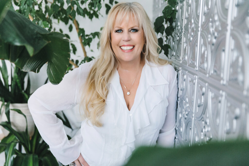 Branding photography session with a woman in a white dress shirt surrounded by green plants and a silver wall.  Photography session by Lindsay Hite. 