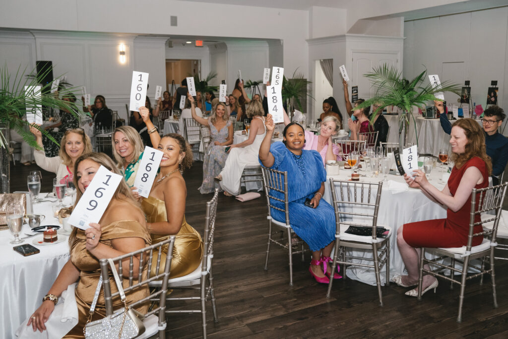 Women in a large room holding live auction signs. 