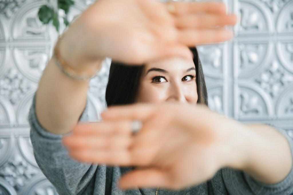 Woman peeking through her hands with a silver backdrop.  Photography by Lindsay Hite